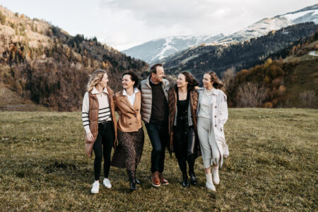 Fünfköpfige Familie geht lächelnd Arm in Arm über eine Bergwiese, schneebedeckte Salzburger Alpen im Hintergrund, herbstliche Stimmung, Familienportrait in der Natur, Familienfotografie Salzburg von Leonie Unterkofler