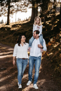 Familie spaziert durch den herbstlichen Wald, Tochter sitzt fröhlich auf den Schultern des Vaters