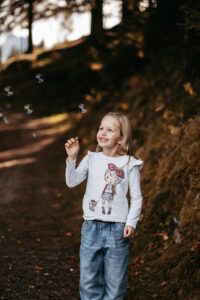Lachendes Mädchen spielt mit Seifenblasen im herbstlichen Wald