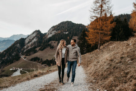 Paar Arm in Arm auf einem Bergweg vor herbstlicher Berglandschaft