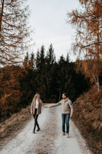 Verliebtes Paar geht Hand in Hand einen Waldweg im herbstlichen Salzburger Land entlang